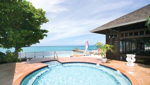 A pool with a view of the ocean, a covered seating area, and a building with a sloped roof. - Grand Decameron Montego Beach, A Trademark All Inc (Montego Bay)