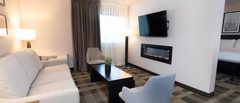 A hotel room with a sofa, a chair, a coffee table, a TV, and a fireplace.