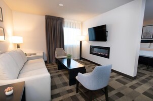 Habitación de hotel con sofá, sillón, mesa de centro, televisor y chimenea.