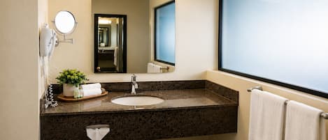 A bathroom with a marble countertop, a sink, a mirror, and a towel rack.