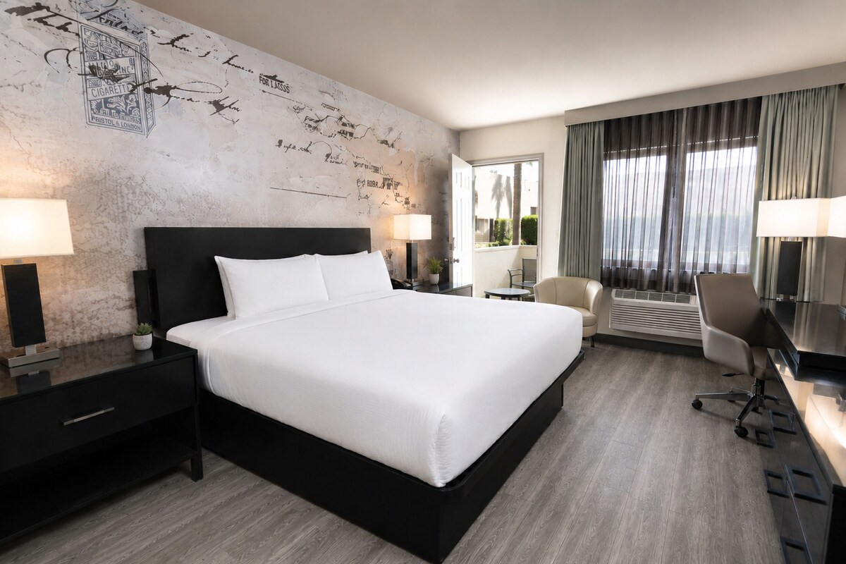 Een hotelkamer met een groot bed, een bureau, een stoel, een bureaulamp, een nachtkastje en een muur met een vintage ontwerp.