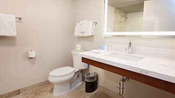 Un baño con inodoro, lavamanos, espejo y un cubo de basura.