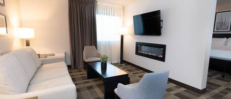 Ein Hotelzimmer mit einer Couch, einem Sessel, einem Couchtisch, einem Fernseher und einem Kamin.