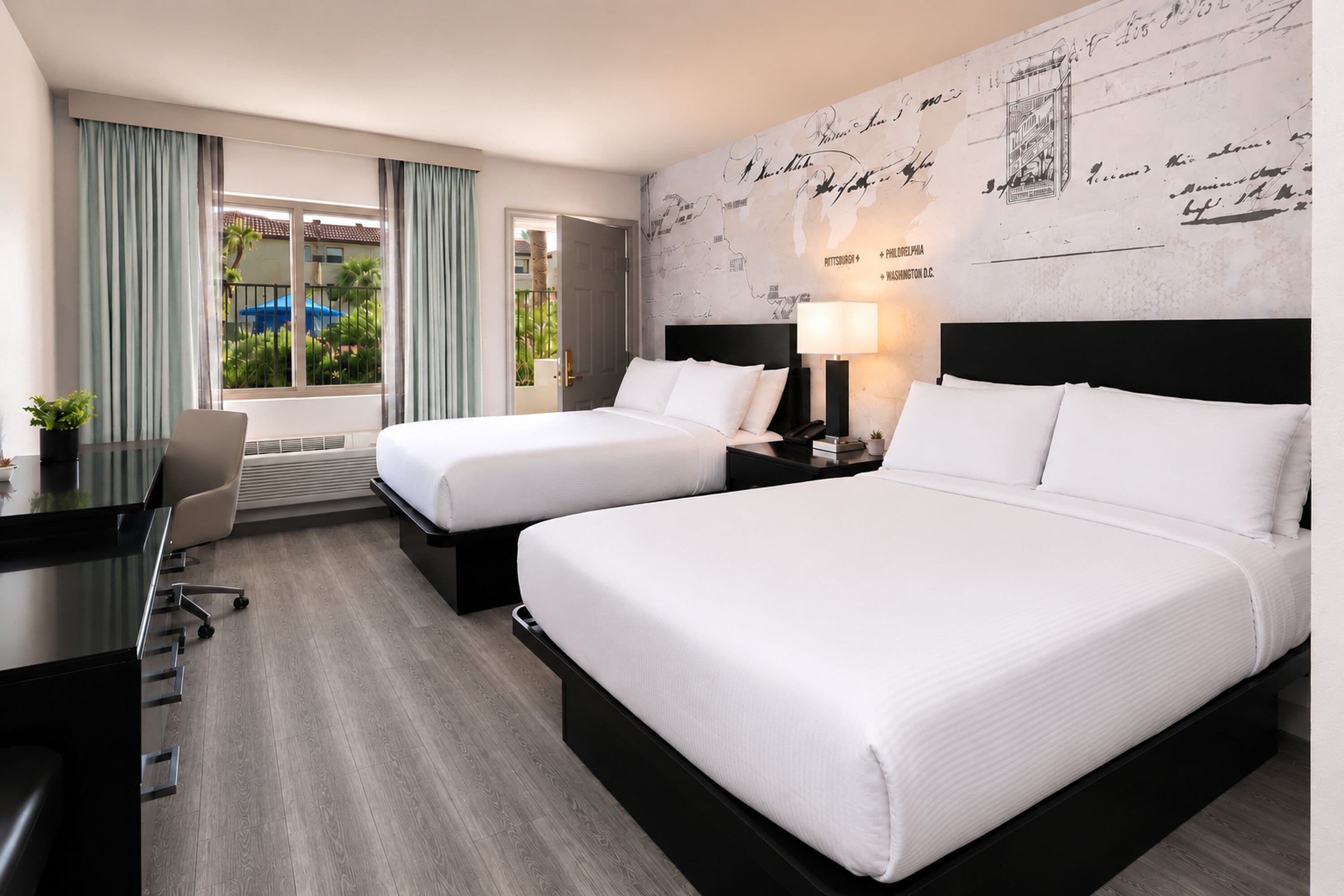 A hotel room with two beds, a desk, and a view of the outdoors.