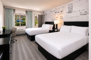 Quarto de hotel com duas camas, uma escrivaninha e vista para o exterior.