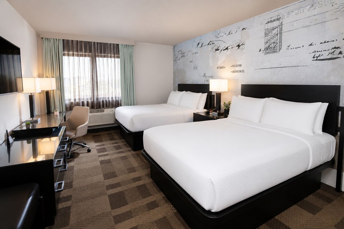 Een hotelkamer met twee bedden, een bureau met stoel, een groot raam met gordijnen en een muur met een kaart.