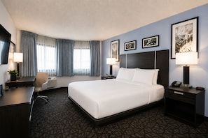 Een hotelkamer met een groot bed, een bureau met een stoel, een bureaulamp, een nachtkastje met een lamp en een aan de muur bevestigde televisie.
