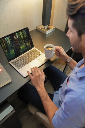 A person using a laptop on a desk with a cup of coffee, a book, and a lamp. - Silver Sevens Hotel and Casino, a Wyndham Garden (Las Vegas)