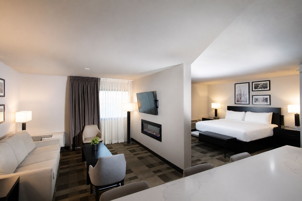 Een hotelkamer met een bed, een bureau, een stoel, een televisie en een raam met gordijnen.