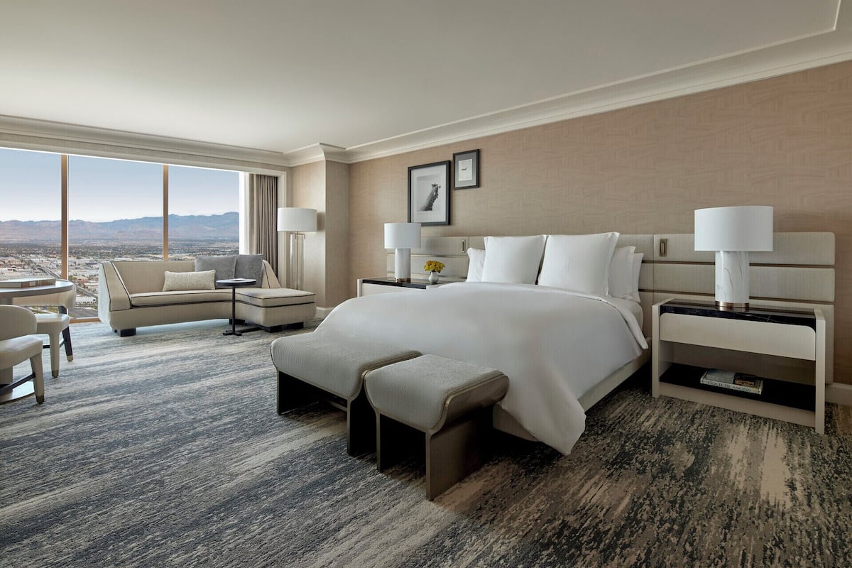 Amplia habitación de hotel con una cama grande, una zona de estar con sofá y sillones, una mesita y vistas a la montaña.