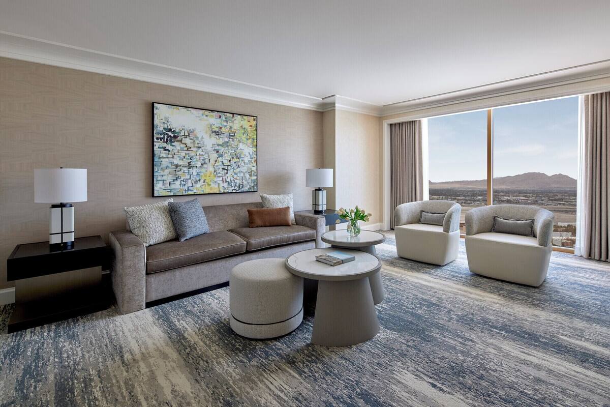 Un hotel moderno con una habitación amplia y ventana que ofrece vistas a la ciudad, un sofá gris, dos sillones, una mesita de café y un cuadro en la pared.