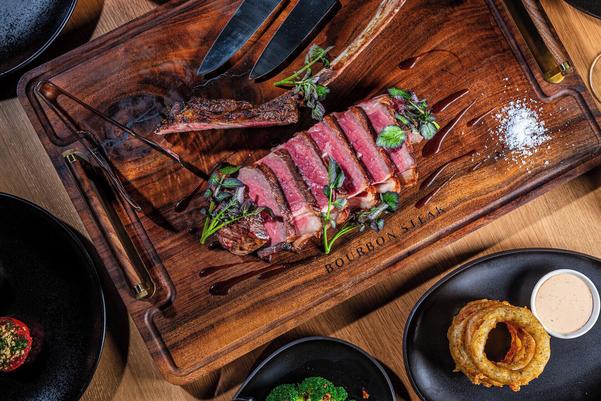 A steak on a wooden board with a knife and fork beside it.