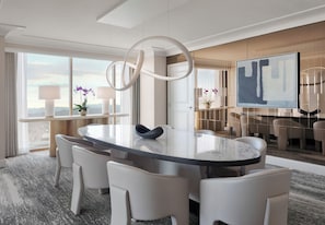 A modern hotel room with a large round table, white chairs, a large window with curtains, a flat-screen TV, and a decorative wall piece.