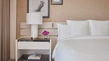 A hotel room with a bed, a nightstand with a lamp, a small table with a vase of flowers, and a framed picture on the wall.