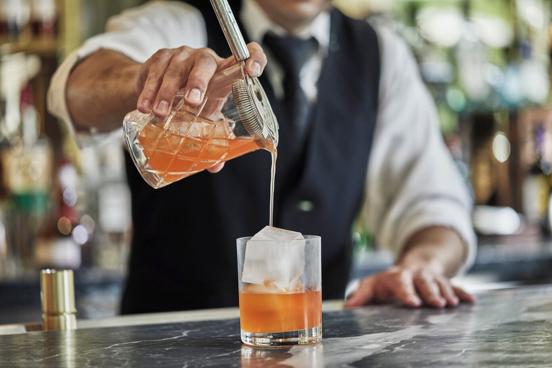 A bartender pouring a drink into a glass with ice.
