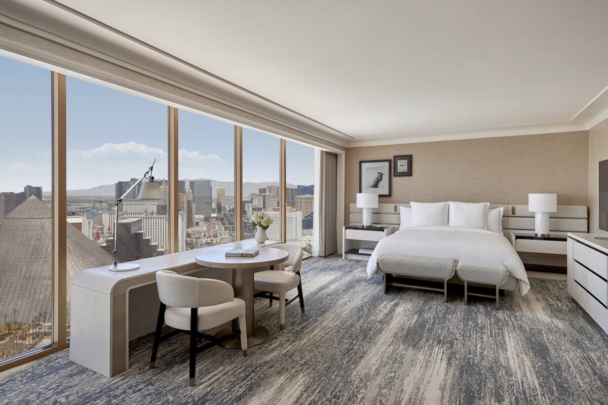 Habitación de hotel con una cama grande, un escritorio con silla, una mesita y vistas a la ciudad.