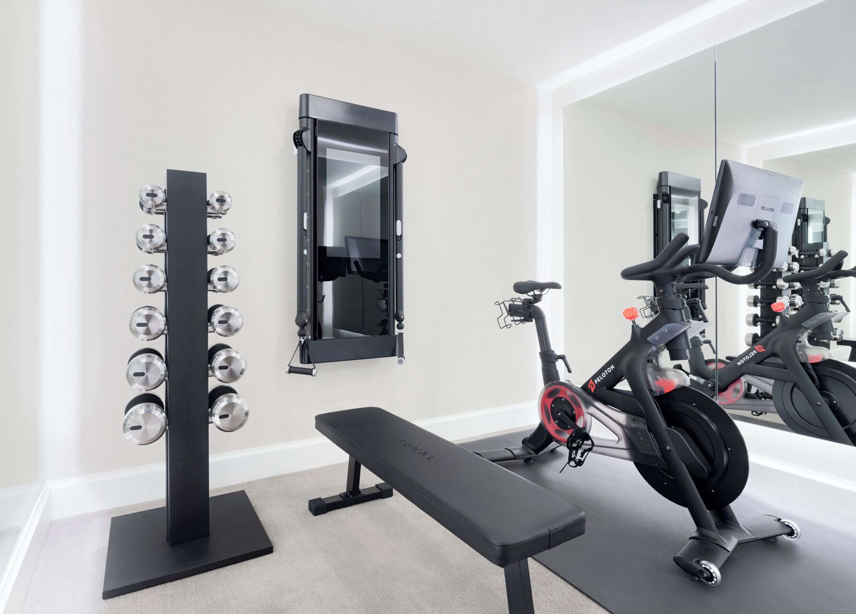 A home gym with a stationary bike, weight bench, and a wall-mounted dumbbell rack.