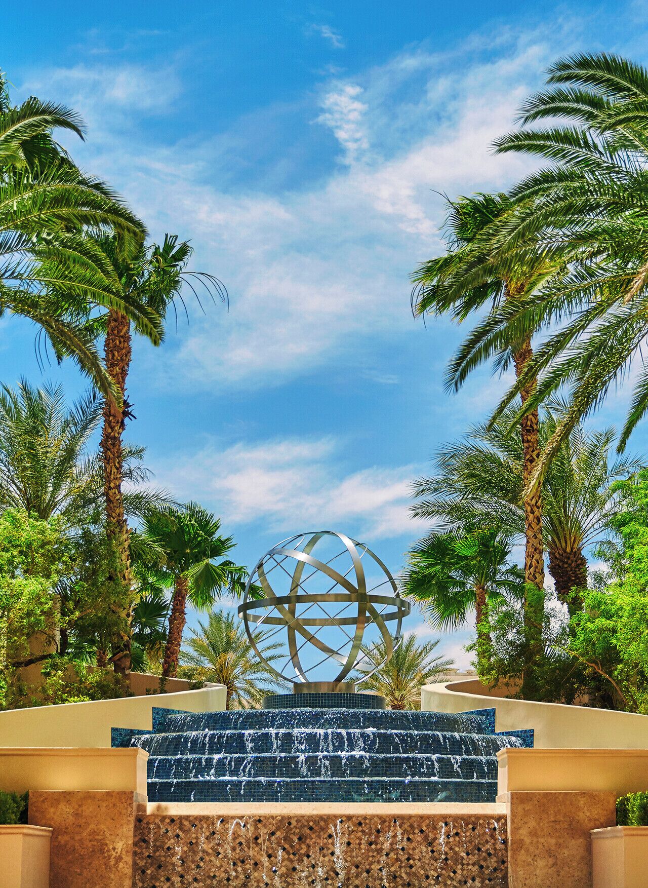 A water feature with a spherical structure in the center, surrounded by palm trees and a clear sky.