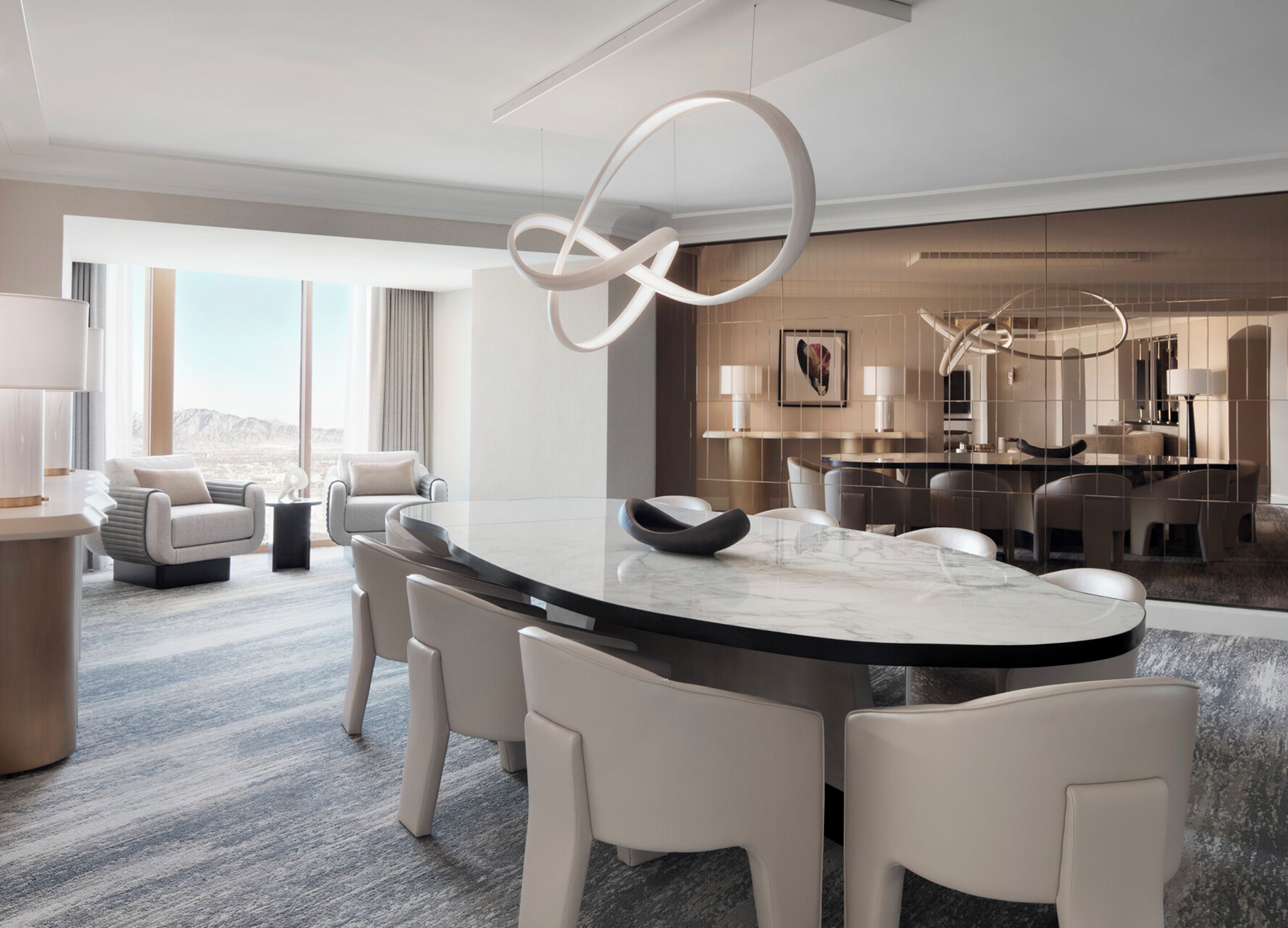 Une chambre d’hôtel moderne avec une grande table à manger ovale, des chaises en cuir blanc et une vue sur les montagnes.