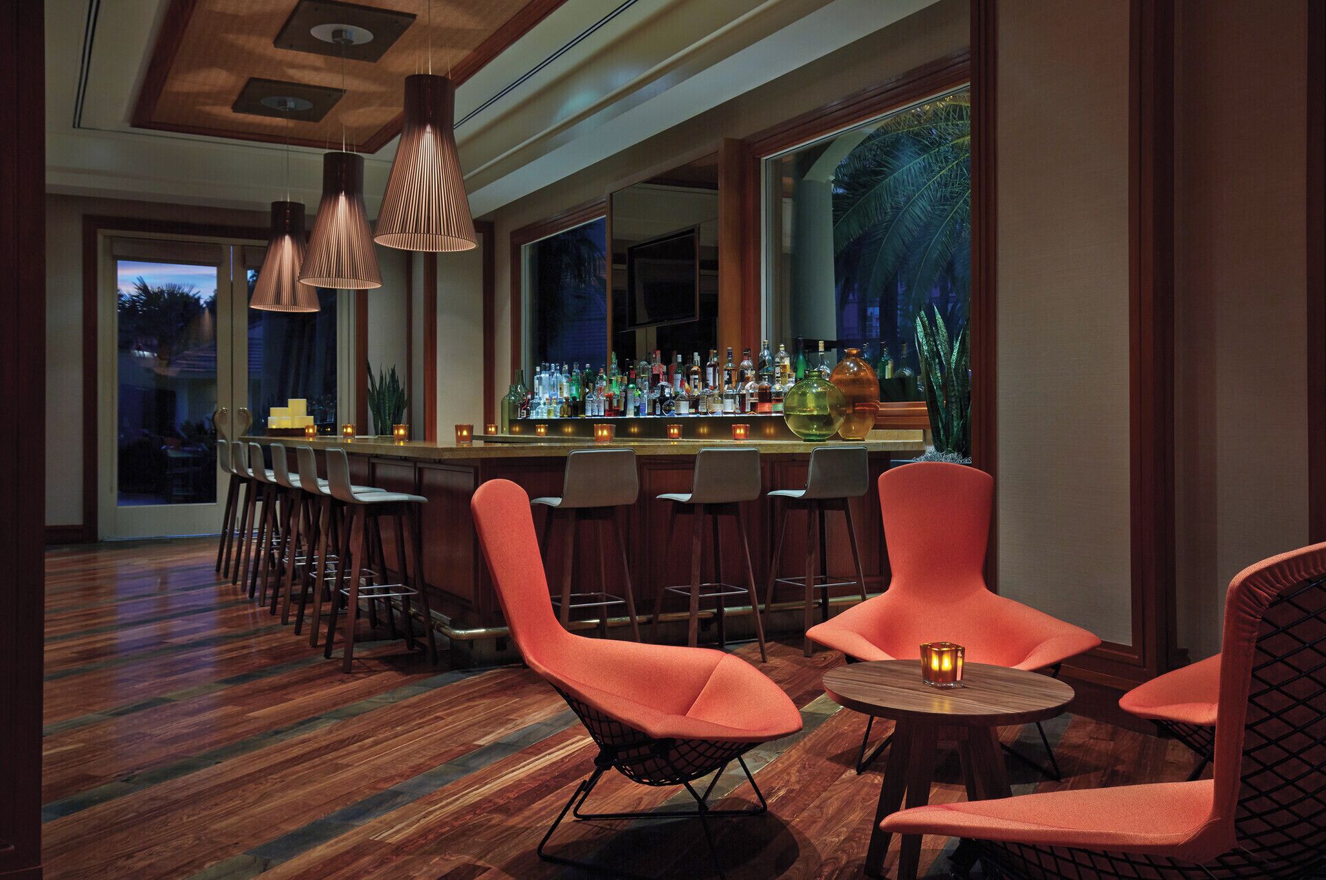A bar area with wooden flooring, multiple bar stools, and a bar stocked with bottles.