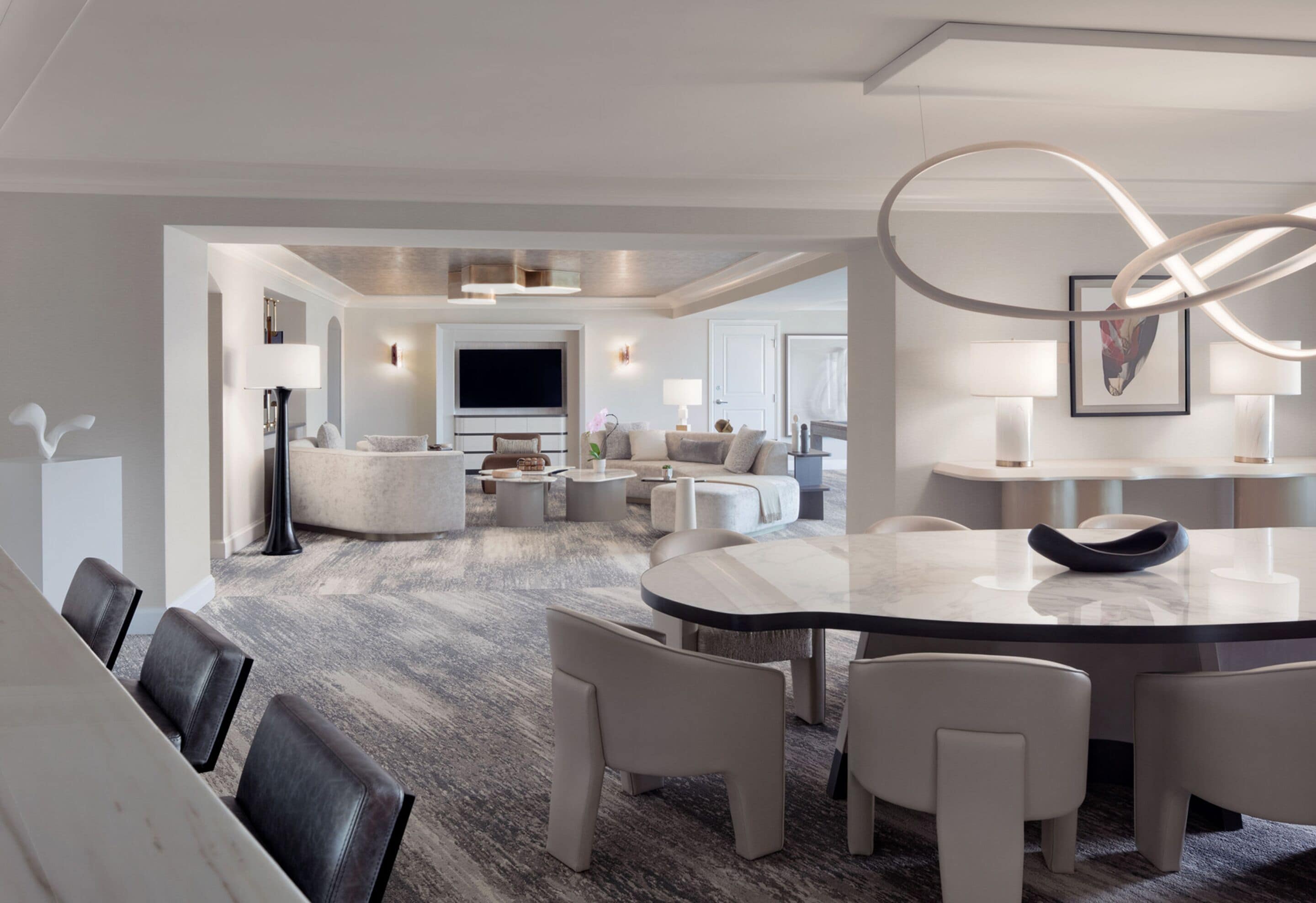 Un espace de repas moderne avec une table en marbre et des chaises blanches, un salon avec des canapés et un téléviseur, et un sol recouvert de moquette.