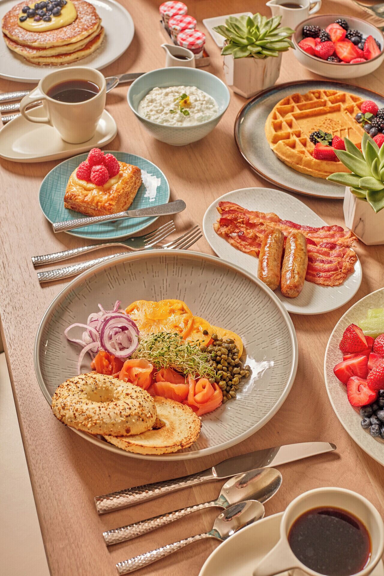 A breakfast buffet with various dishes including pancakes, waffles, bagels, smoked salmon, and fresh fruits.