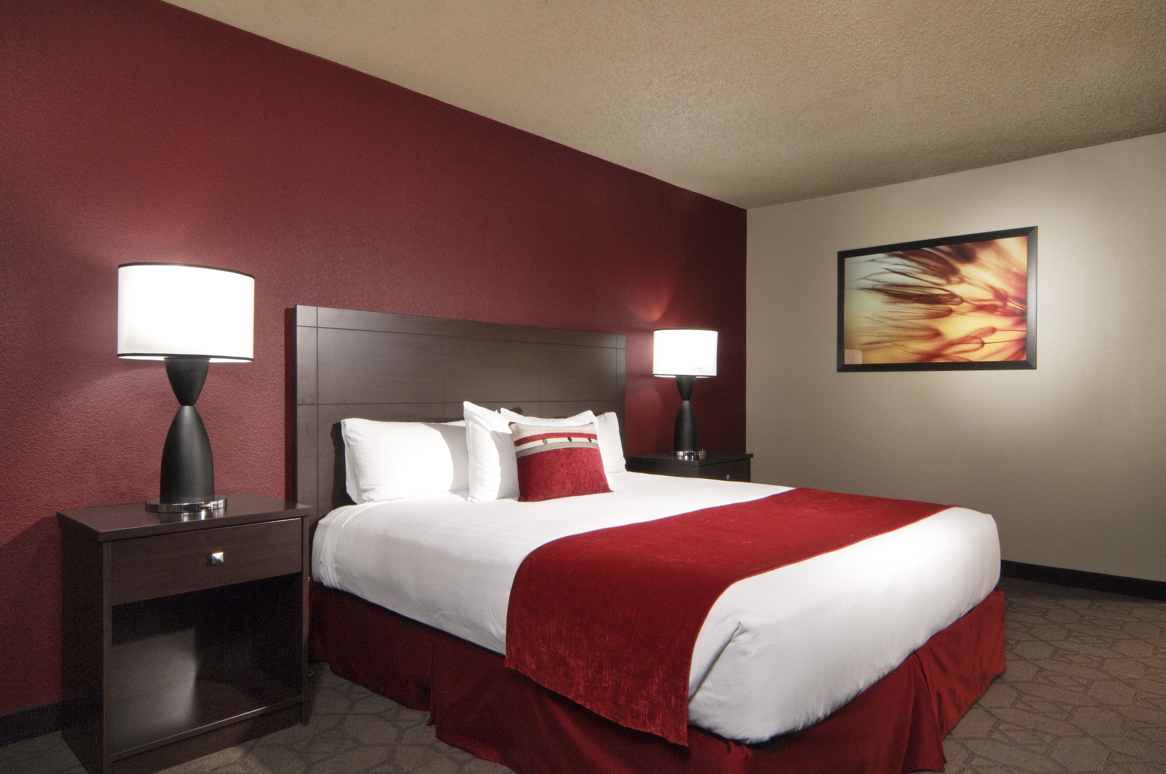 A hotel room with a large bed, two bedside tables, a headboard, a wall-mounted painting, and a carpeted floor.