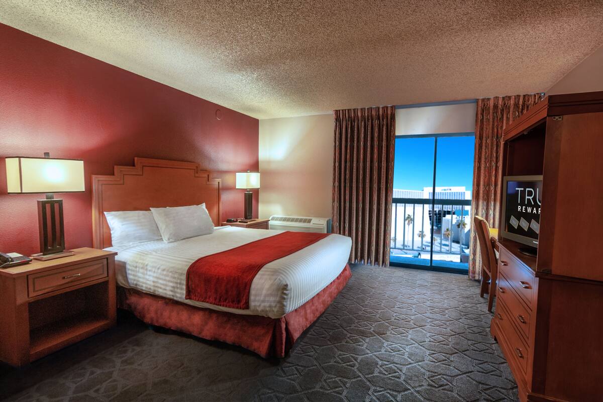 A hotel room with a large bed, two bedside tables with lamps, a TV, and a view of a building through a window with curtains.