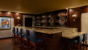 Un espace bar doté d’un comptoir en granit, de tabourets de bar et d’étagères remplies de bouteilles et de verres.