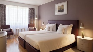 A hotel room with two beds, a desk, a chair, and a nightstand with lamps.
