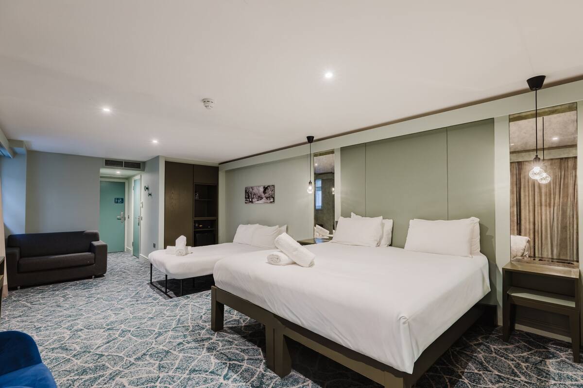 A hotel room with a large bed, a sofa, a desk, and a mirror.