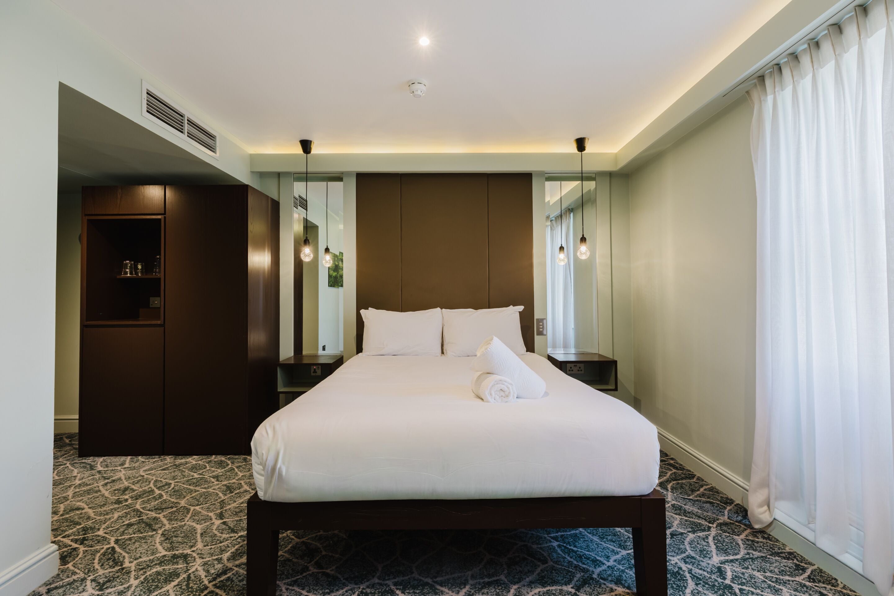 A hotel room with a large bed, a wardrobe, a mirror, and a window with curtains.