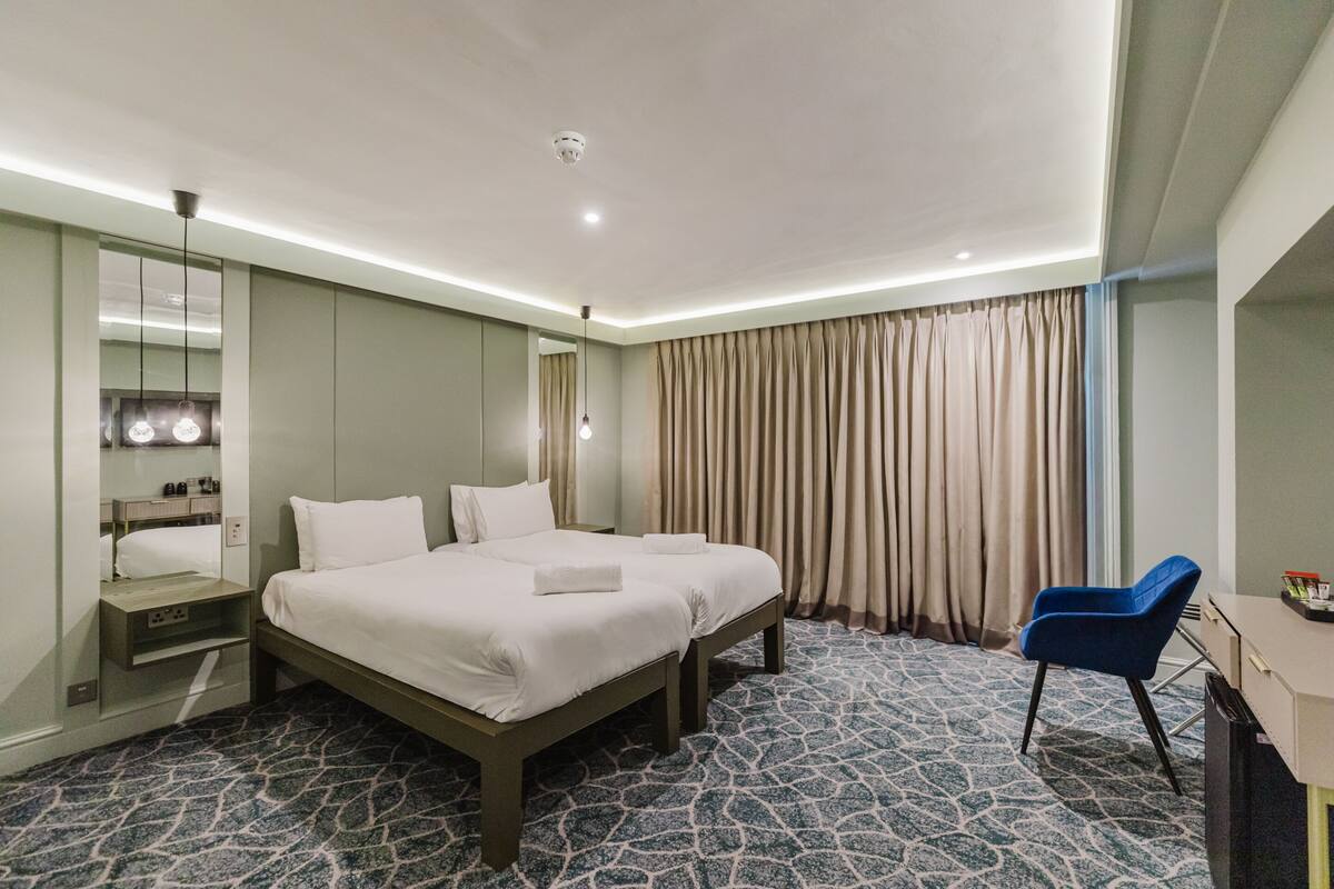 A hotel room with a large bed, a desk, a chair, a mirror, and a window with curtains.