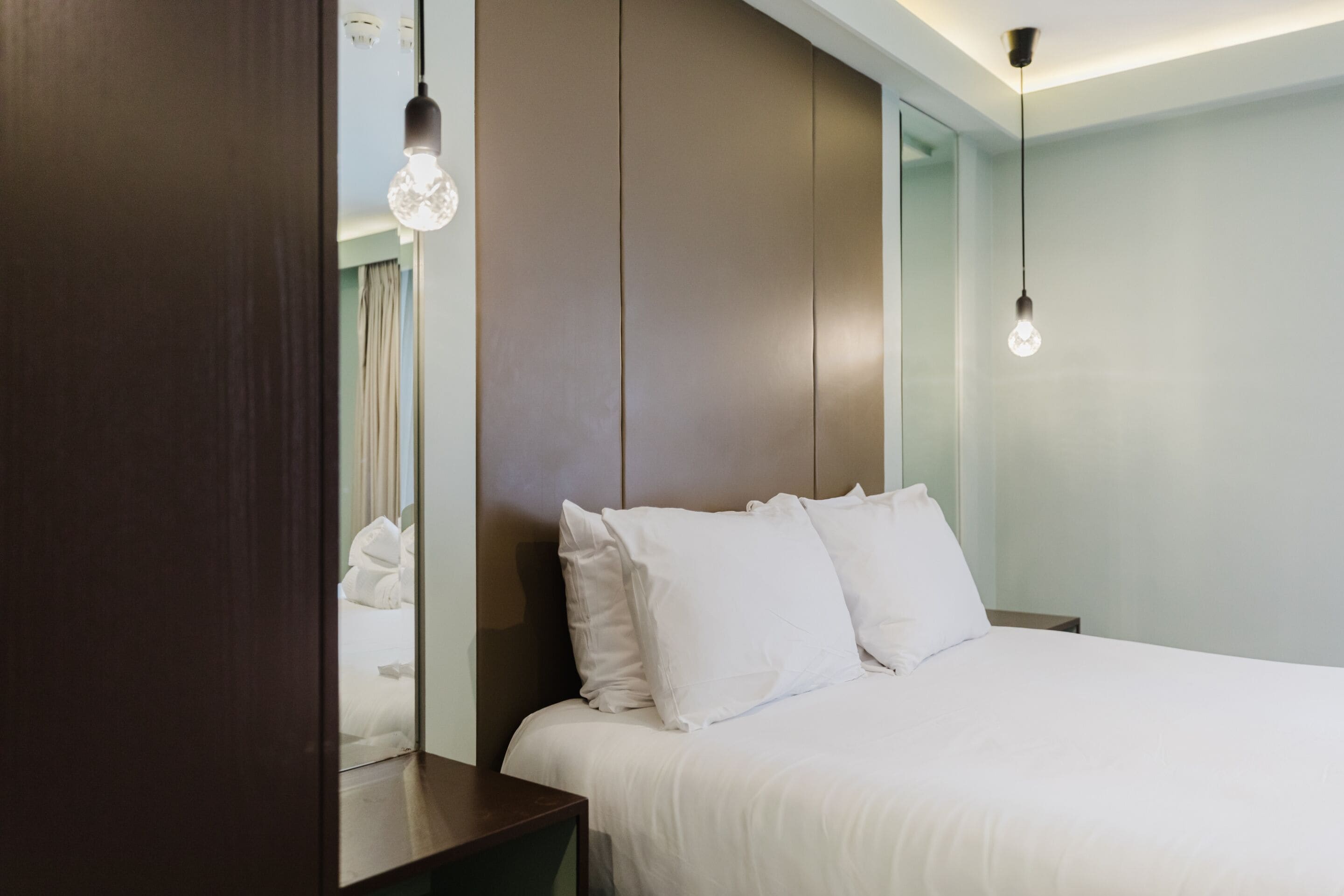 A modern hotel room with a large bed, a wooden headboard, and pendant lighting.