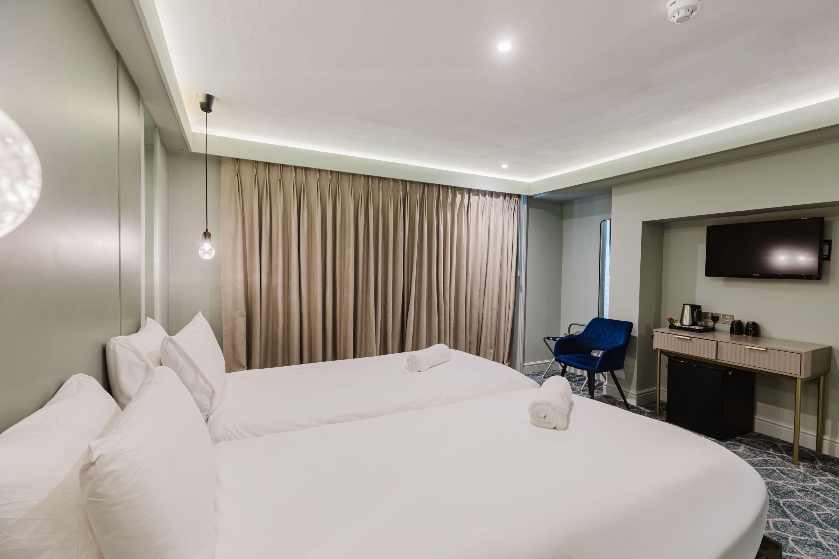 A hotel room with a large bed, a desk, a chair, a television, and a curtain.