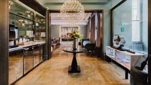 Un hall de hotel con una mesa redonda, una araña, una exhibición de flores y una vitrina con objetos.