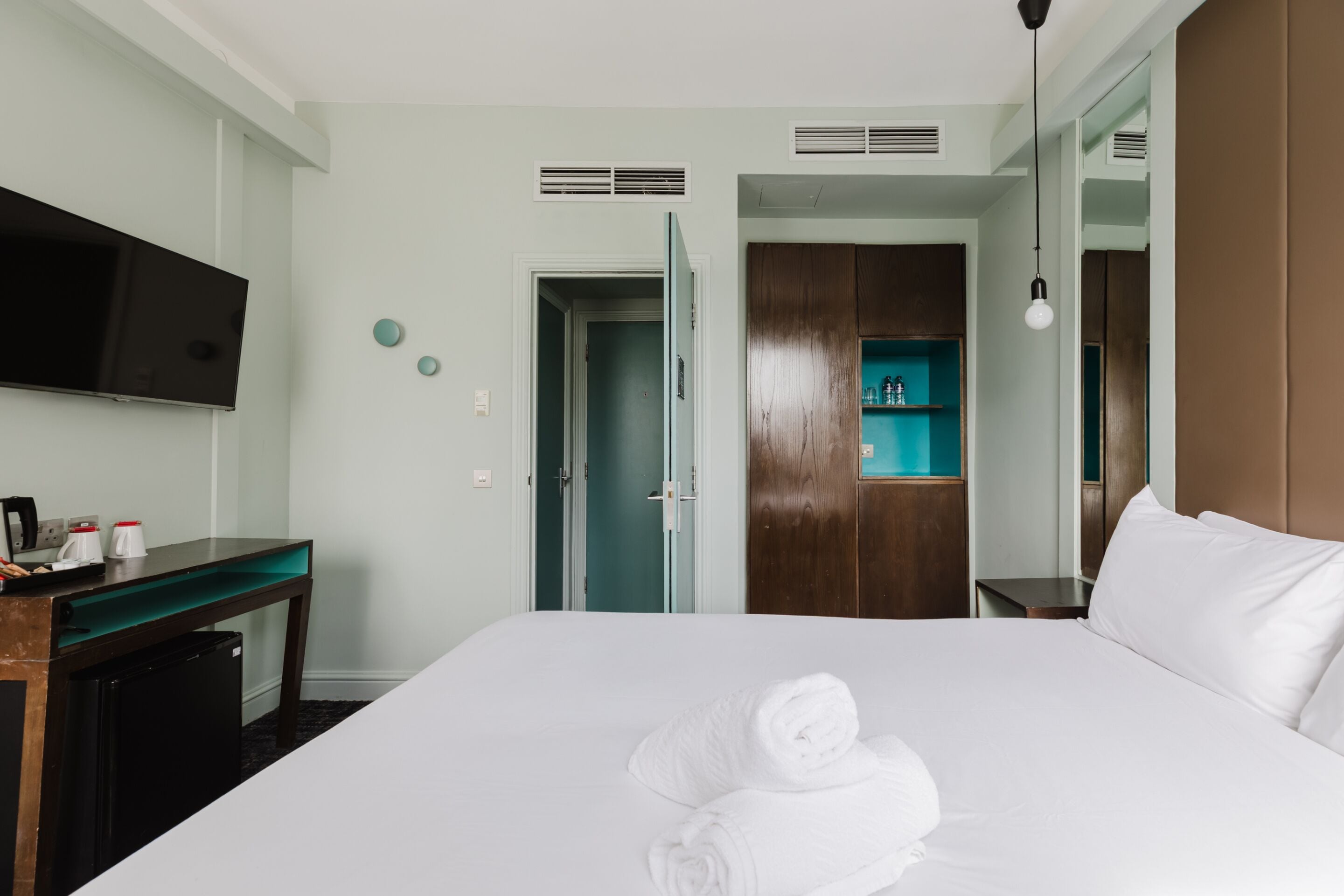 A hotel room with a bed, a desk, a television, a wardrobe, and a bathroom door.