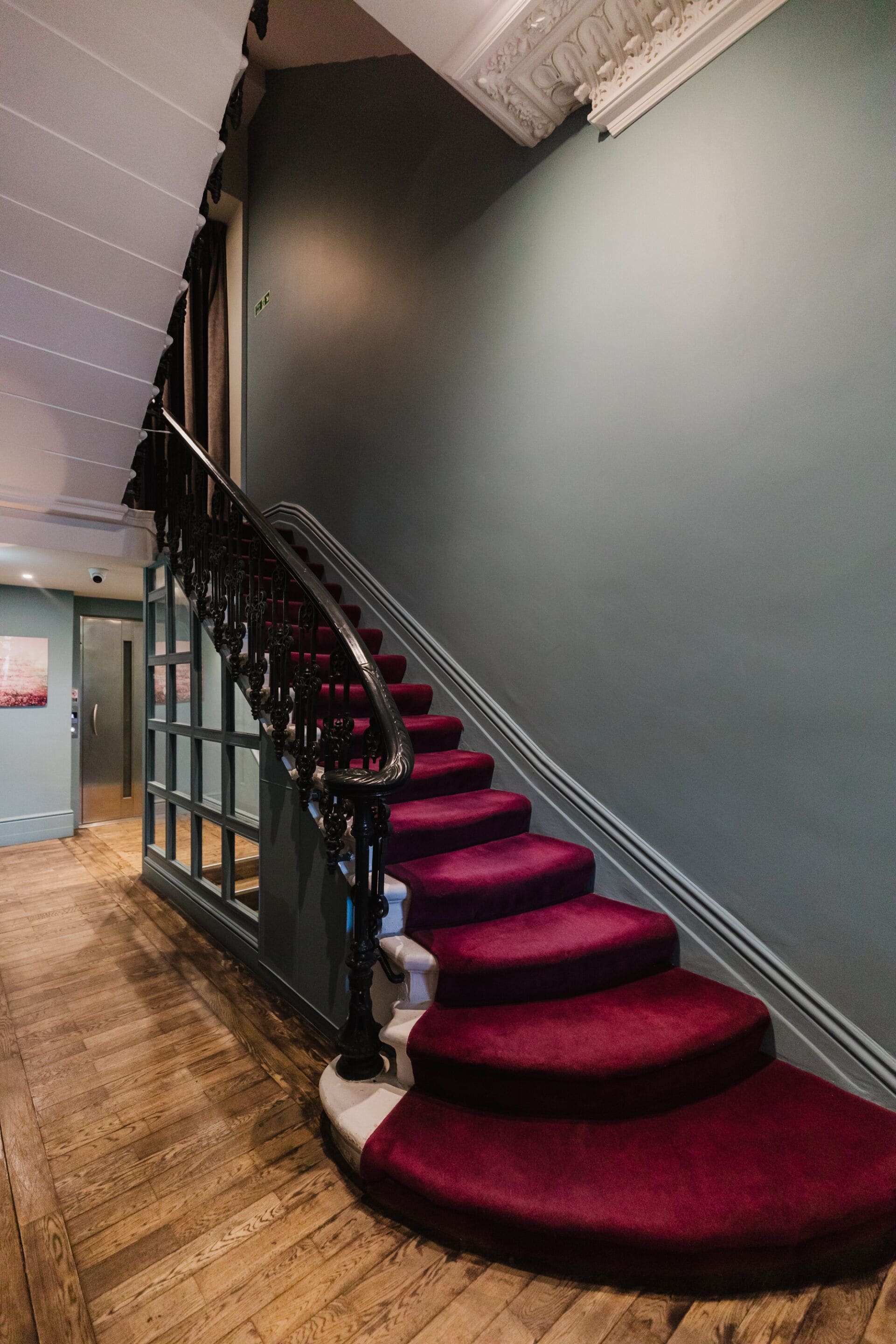 A staircase with red carpeted steps and a black handrail, leading to a door with a glass panel.