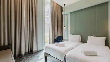 A hotel room with two beds, a large window with curtains, a blue chair, and a patterned floor.