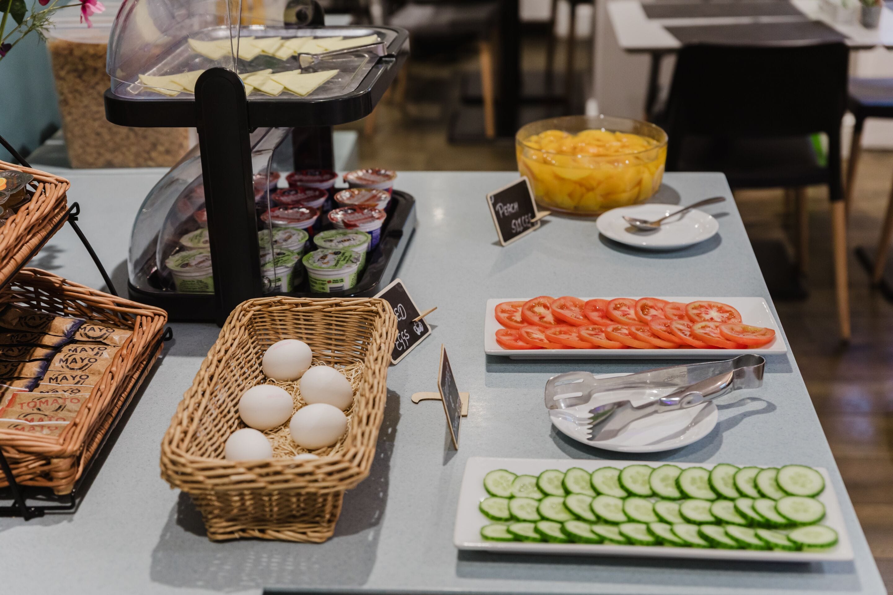 A buffet table with various food items including eggs, tomatoes, cucumbers, and a bowl of fruit.