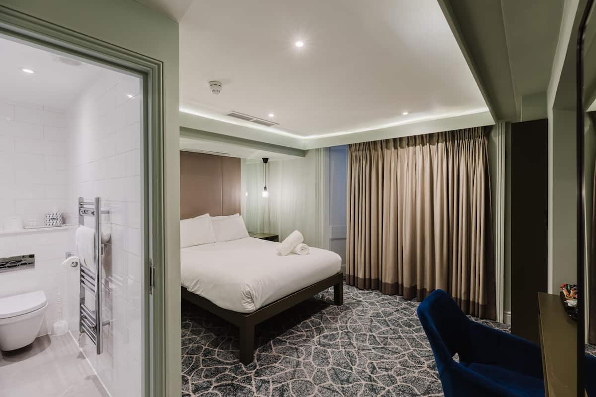 A hotel room with a bed, a shower, a chair, and a desk.