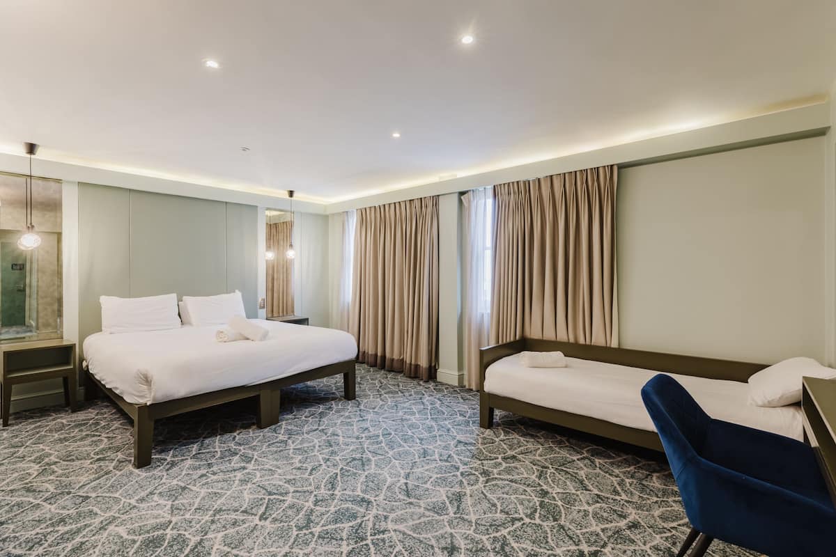 A hotel room with two beds, a desk, a chair, a mirror, and a patterned carpet.