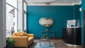A modern lobby with a teal accent wall, a yellow sofa, a glass coffee table, and a reception desk. - Paddington Park Hotel (London)