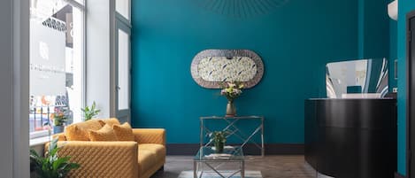 Un'accogliente hall moderna con una parete verde acqua, un divano giallo, un tavolino da caffè in vetro e una reception.