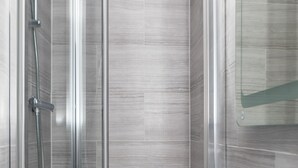A modern bathroom with a glass-enclosed shower, a white sink, and a mirror above it. - Paddington Park Hotel (London)