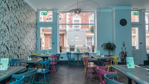 A restaurant with colorful chairs and tables, a herringbone floor, and a view of the street outside. - Paddington Park Hotel (London)