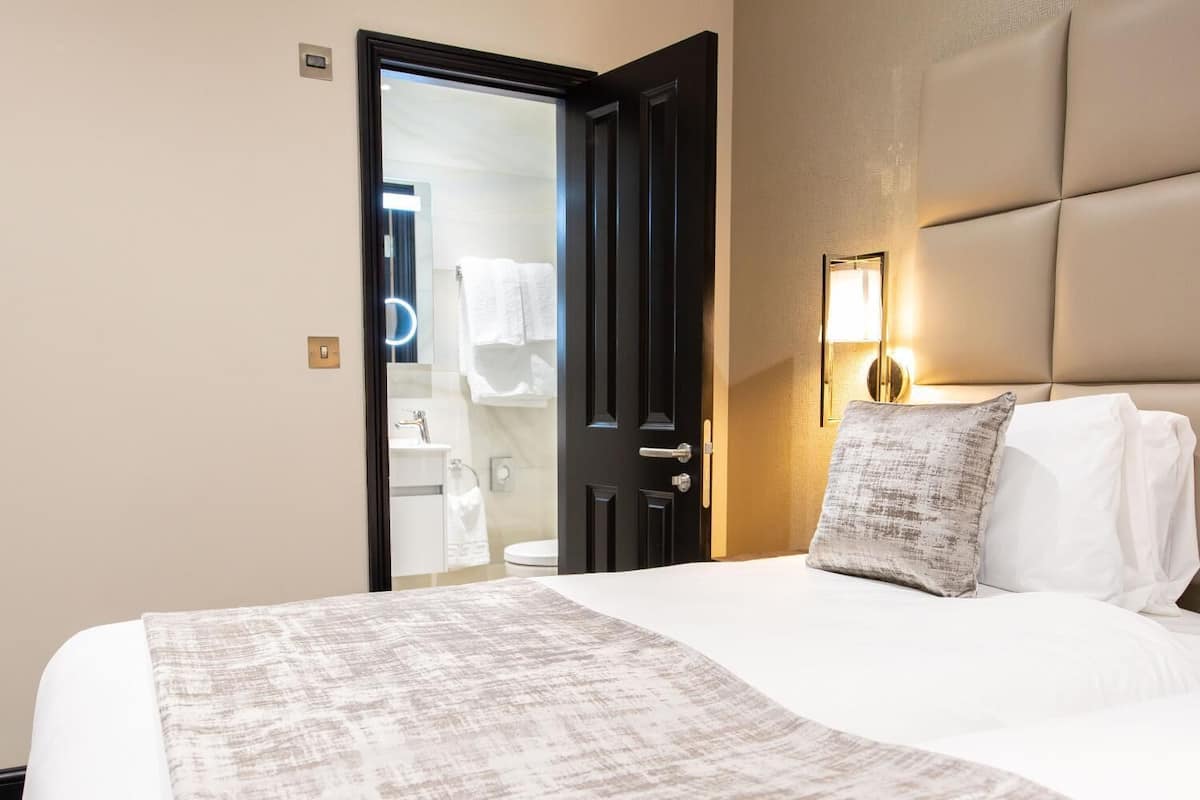 A hotel room with a bed, a bedside lamp, a pillow, and a door leading to a bathroom.