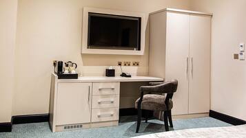 Una habitación de hotel con escritorio, silla, televisor y armario.