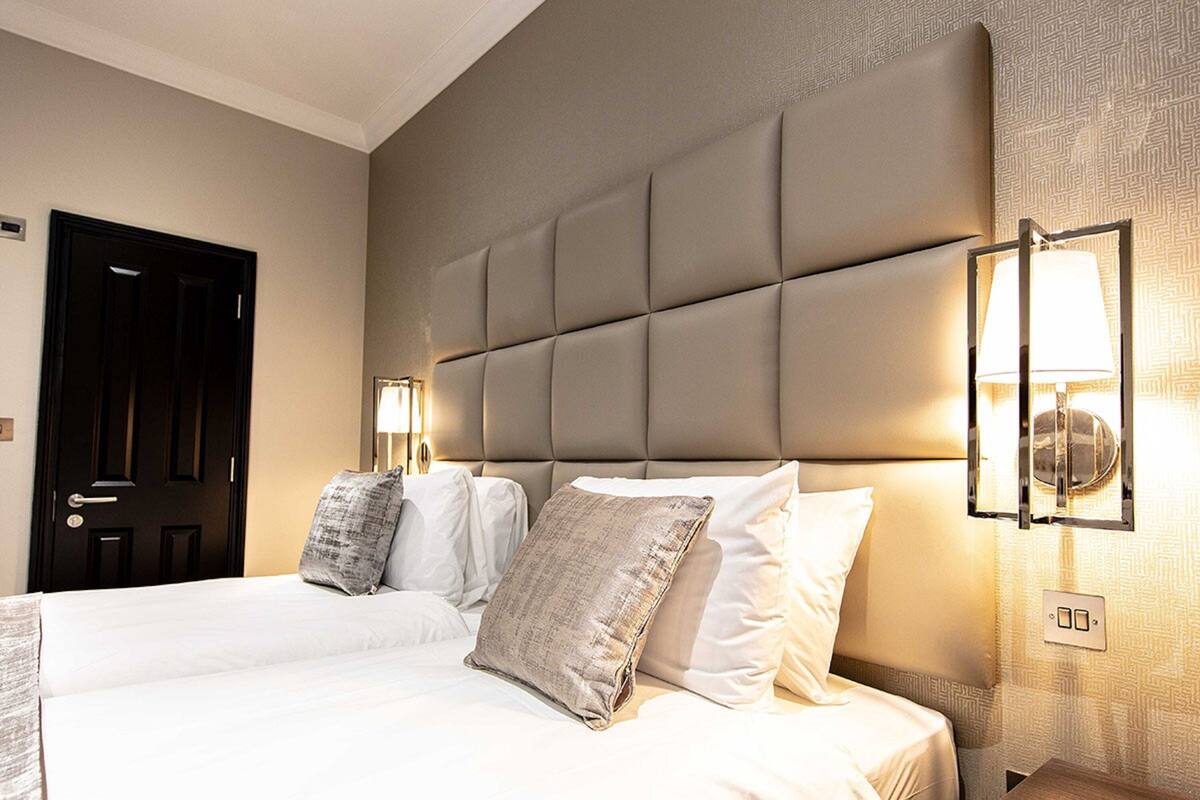 A hotel room with a large bed, a headboard, bedside lamps, and a door.