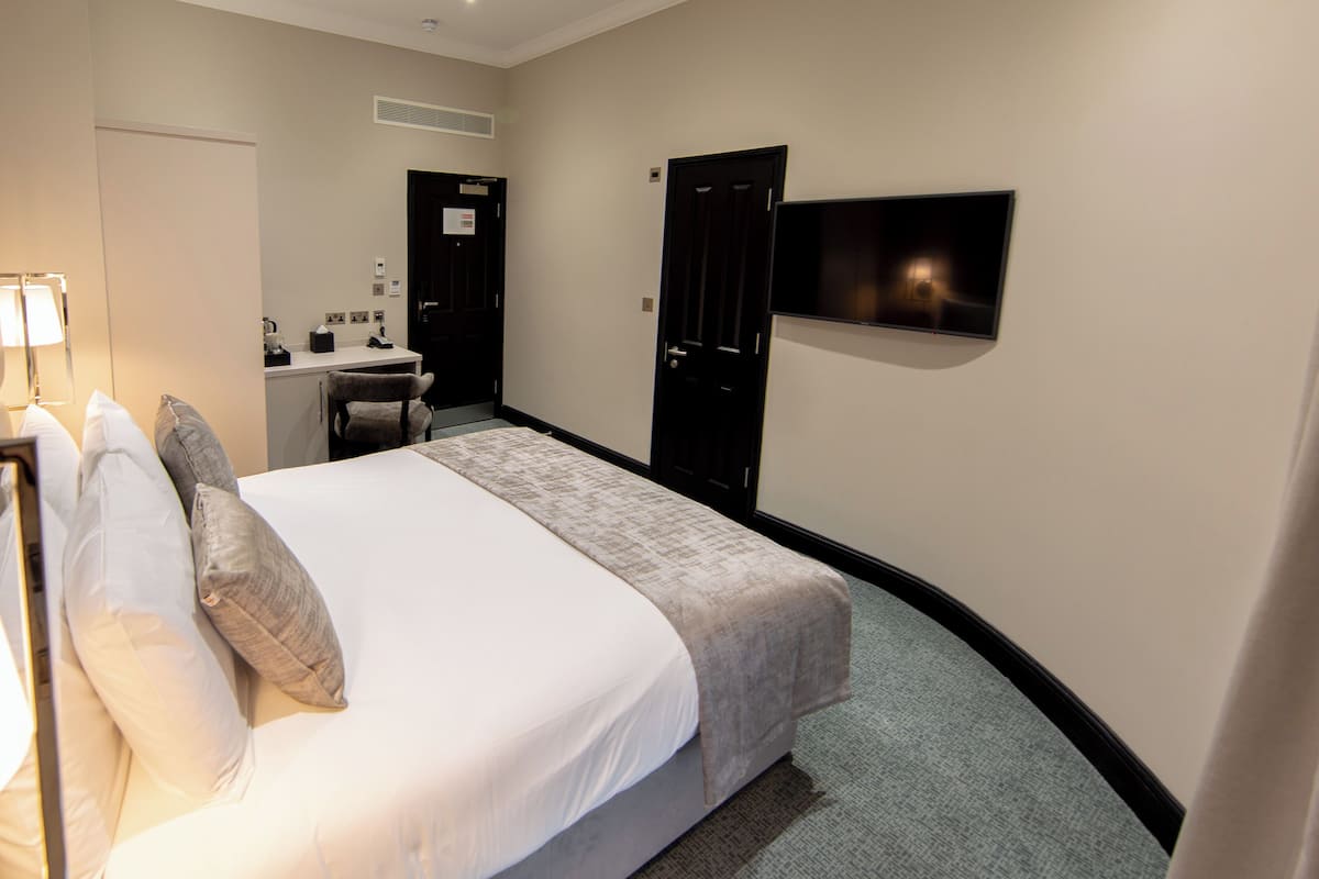 A hotel room with a bed, a desk, a chair, a TV, and a door.